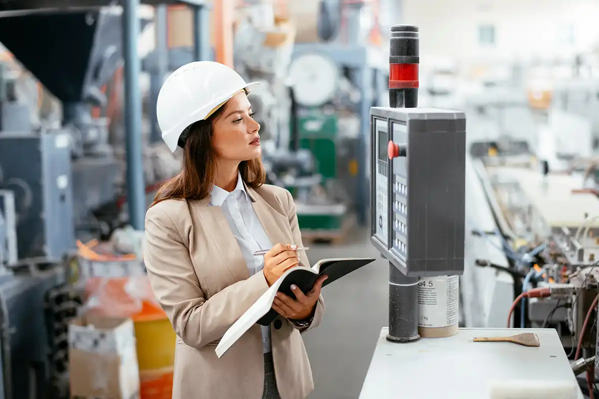 Portrait of businesswoman in factory. Young female architect with helmet in suit.